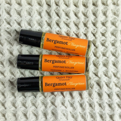 Closeup of 3 Bergamot + Tangerine Perfume Rollers laying on a soft white background.