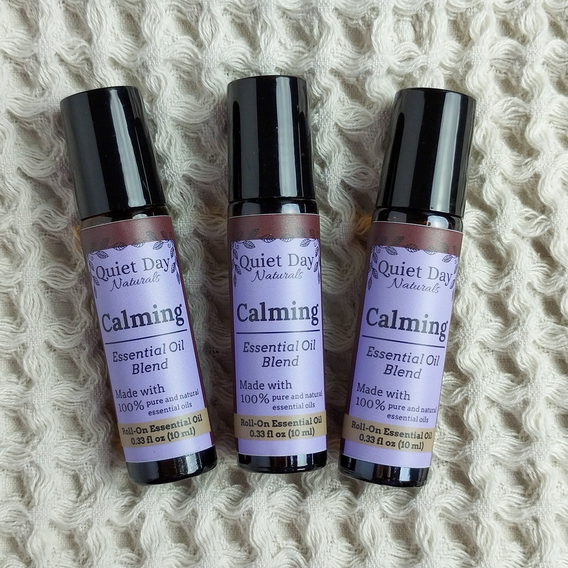 Three Calming Essential Oil Rollers against a soft waffle-textured blanket.