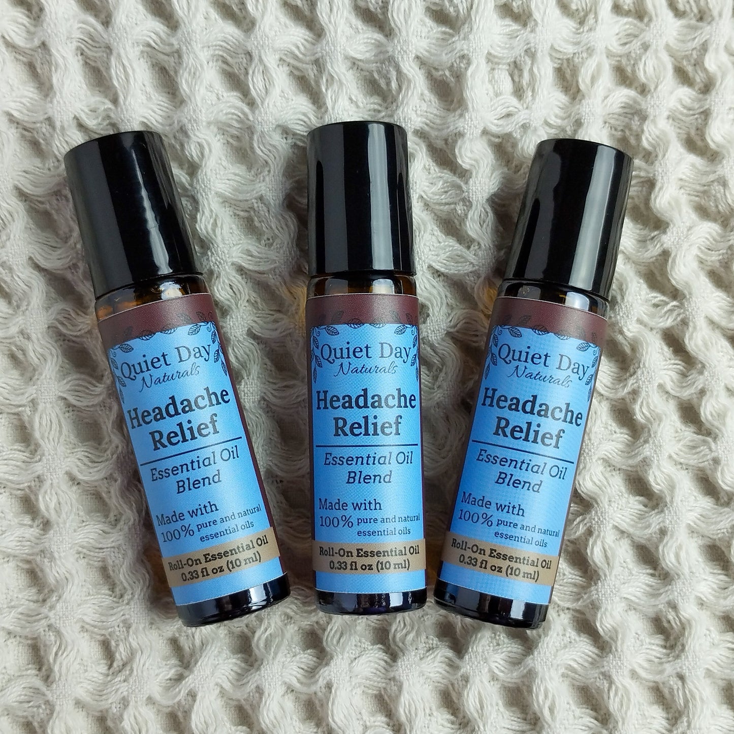 Three Headache Relief Essential Oil Rollers against a soft waffle-textured blanket.