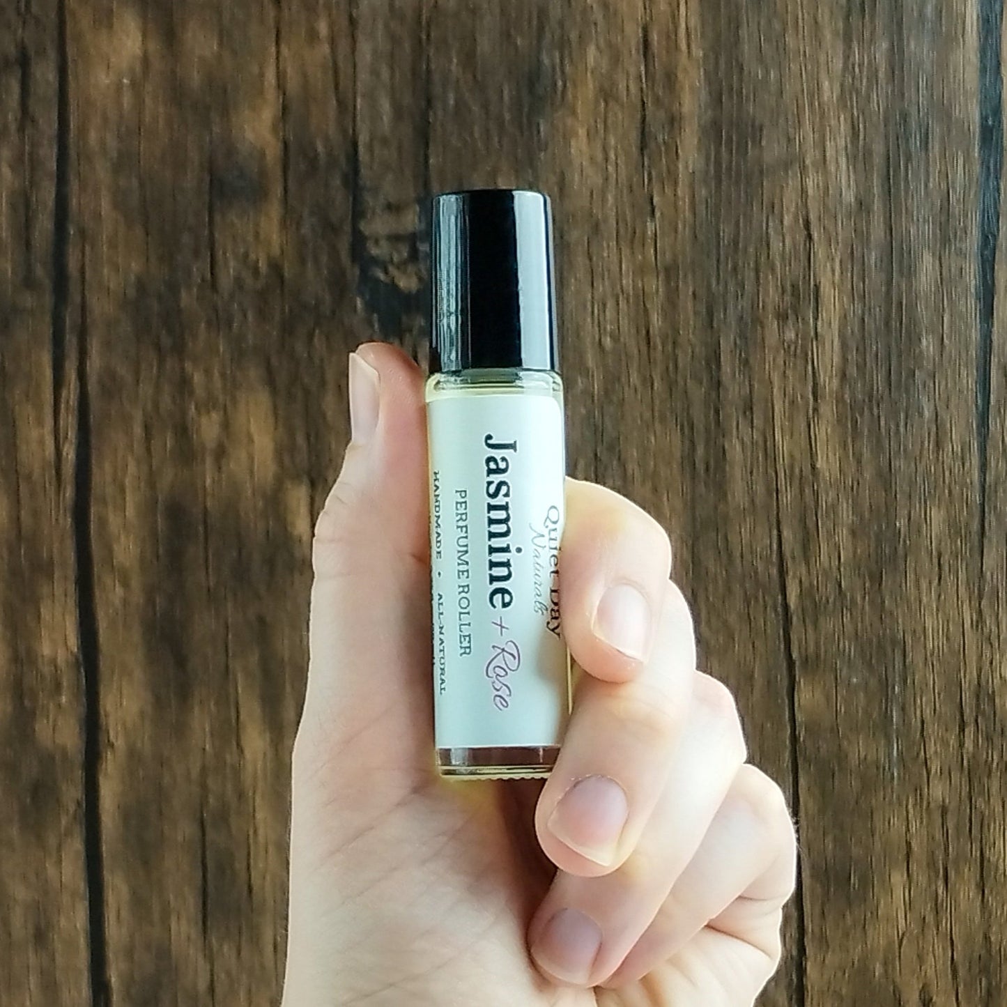 Natural Perfume Roller being held in hand against a wood background.