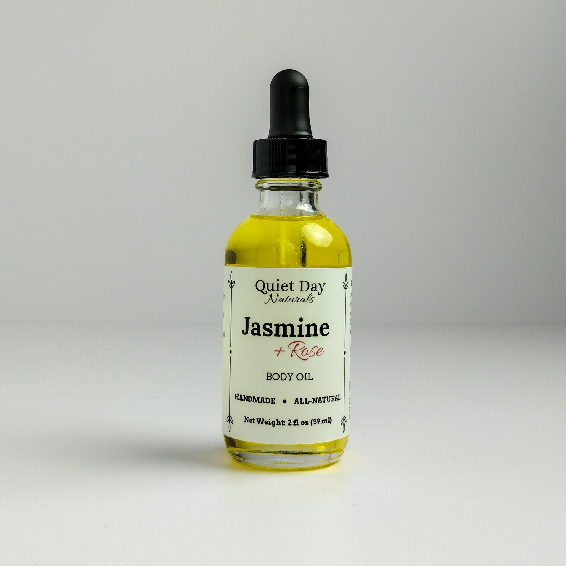 Jasmine and Rose Body Oil in a 2oz glass bottle with dropper standing against a white background.