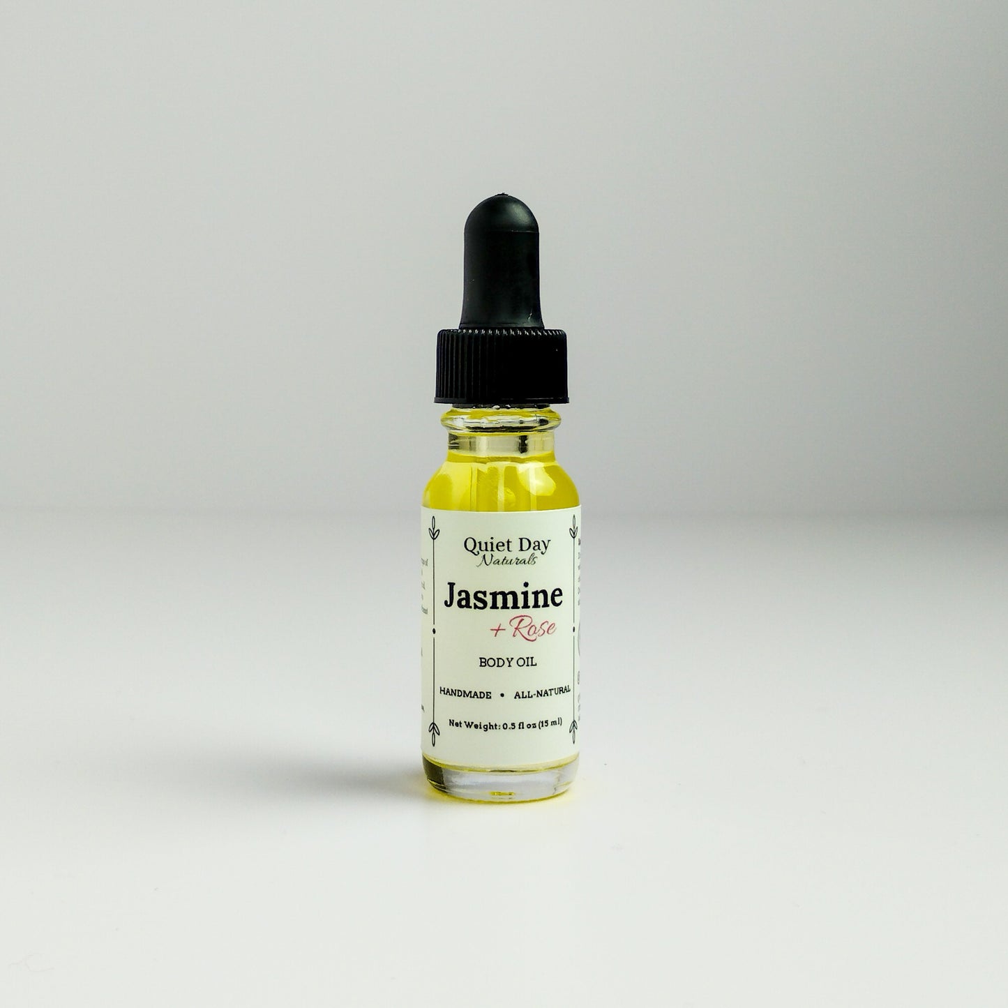 Jasmine and Rose Body Oil in a 0.5oz sampler glass bottle with dropper standing against a white background.