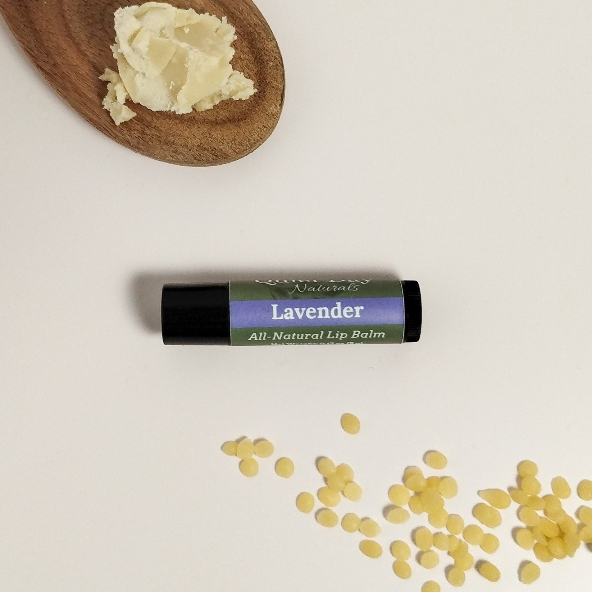 Lavender lip balm sitting on a white background with shea butter and beeswax around it.