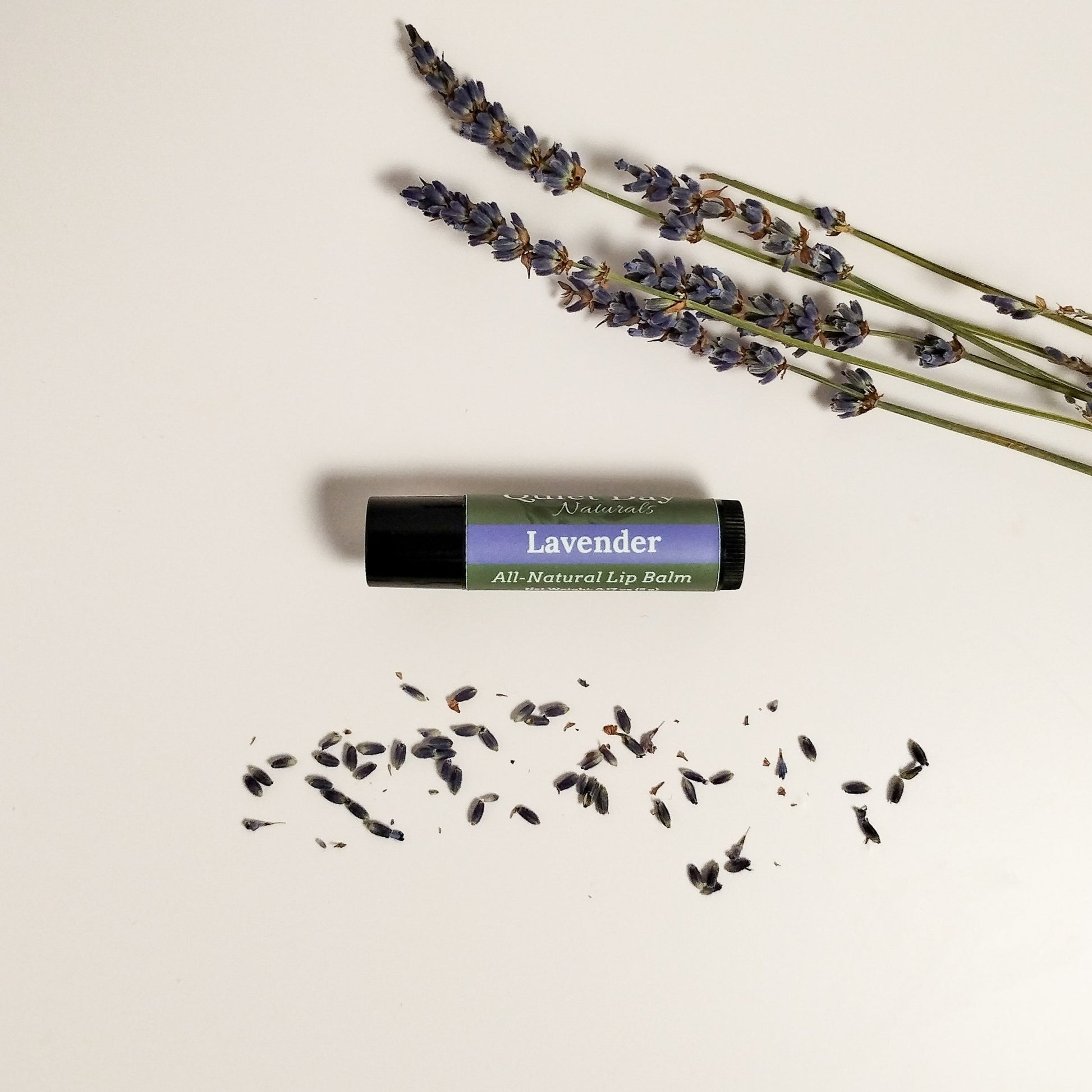Handmade Natural Lip Balm laying on a white background with lavender buds next to it.