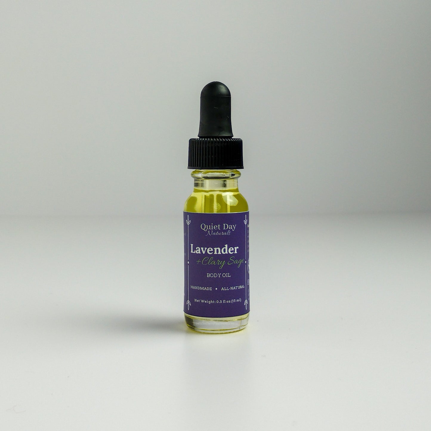 Lavender and Clary Sage Body Oil in a 0.5oz sampler glass bottle with dropper standing against a white background.