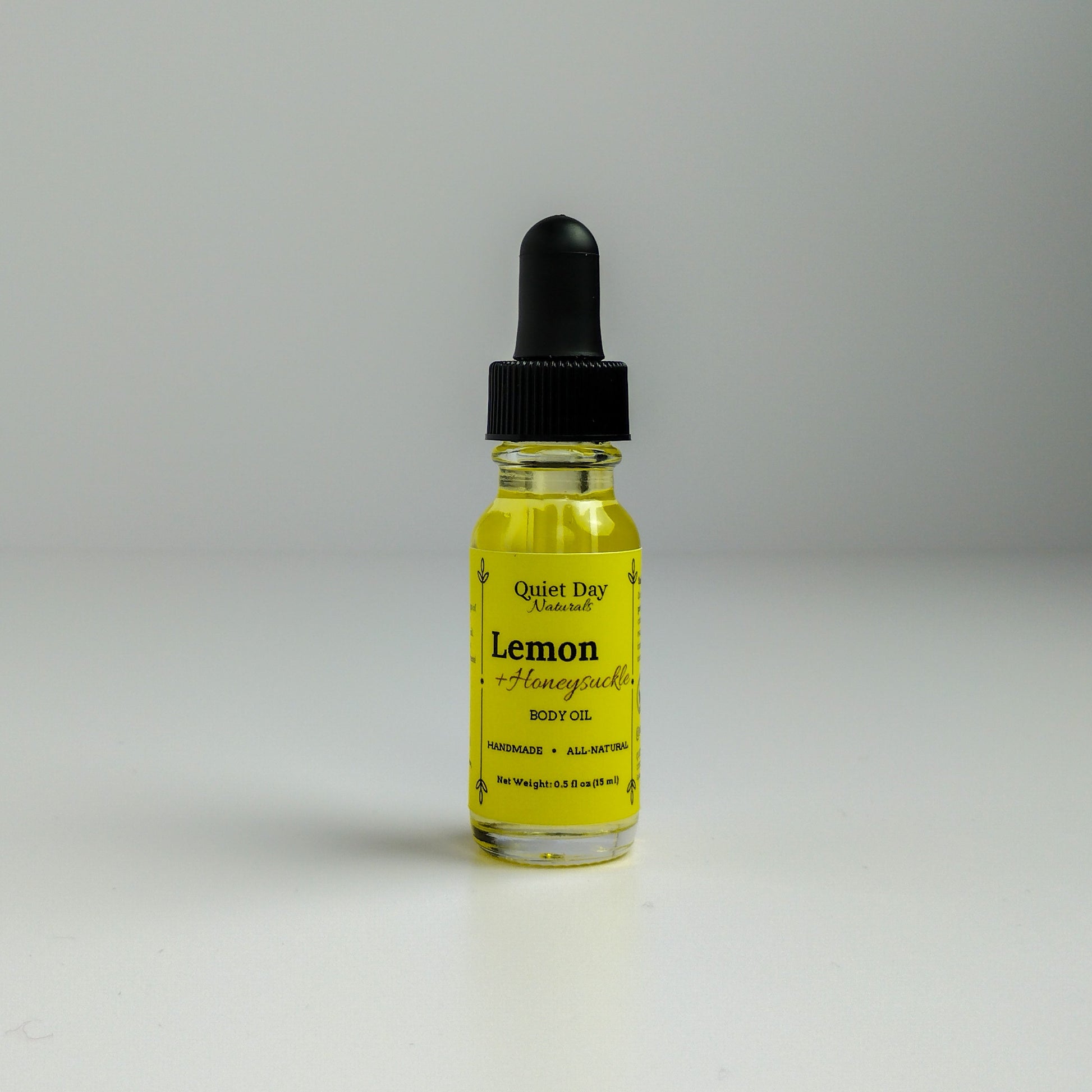 Lemon and Honeysuckle Body Oil in a 0.5oz sampler glass bottle with dropper standing against a white background.