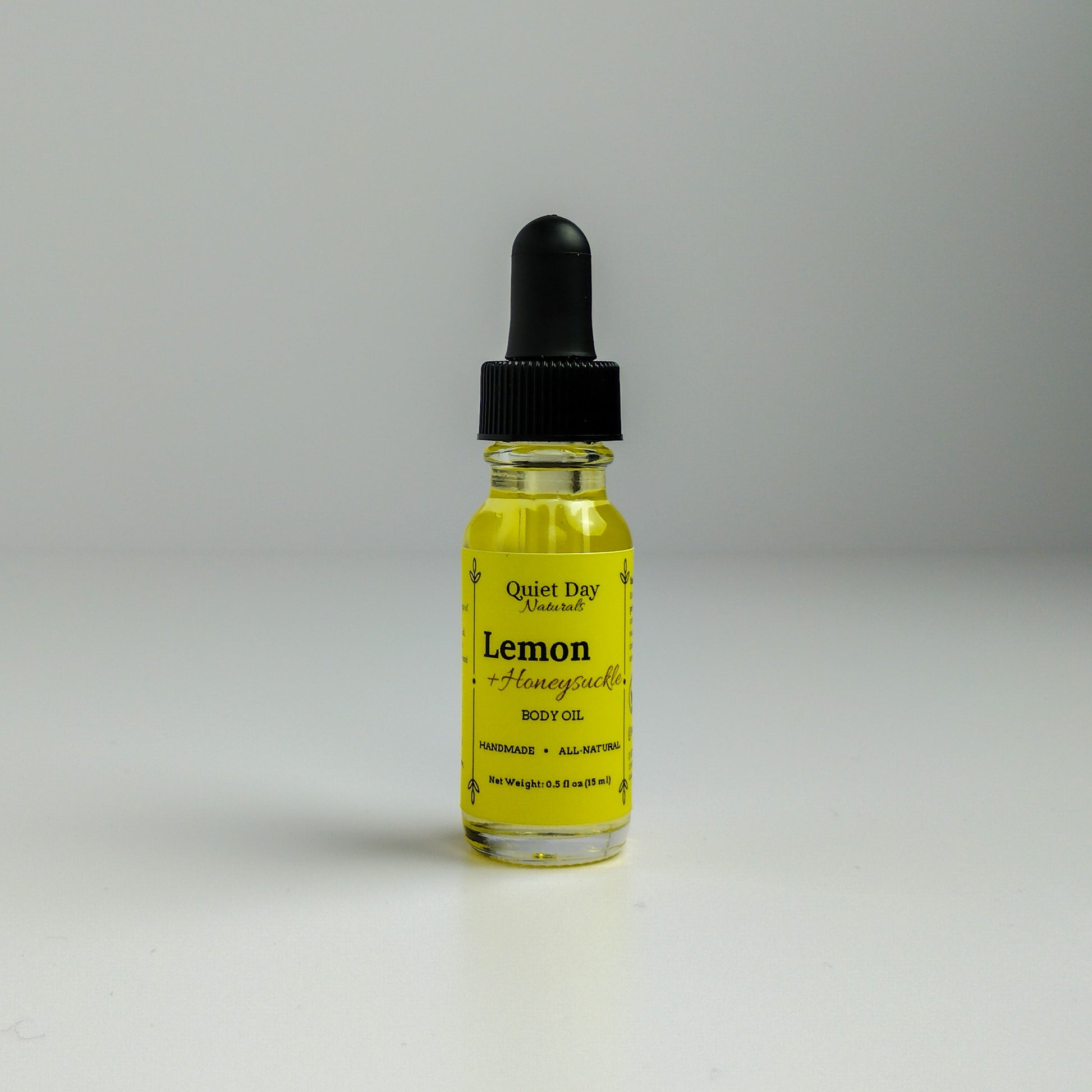 Lemon and Honeysuckle Body Oil in a 0.5oz sampler glass bottle with dropper standing against a white background.