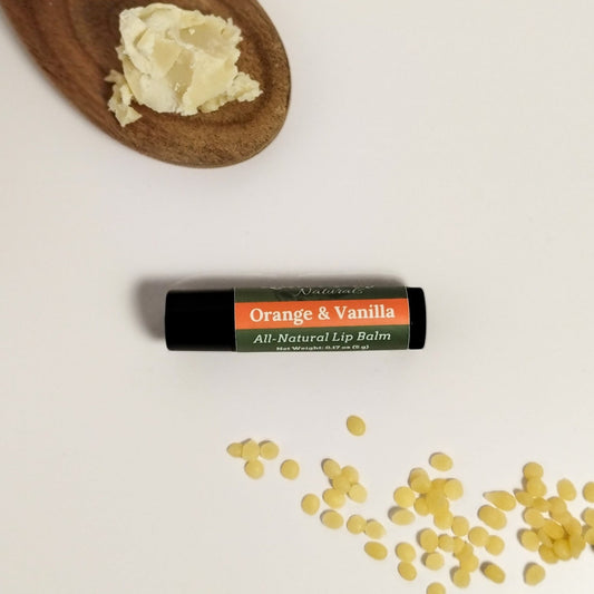 Orange and Vanilla lip balm sitting on a white background with shea butter and beeswax around it.