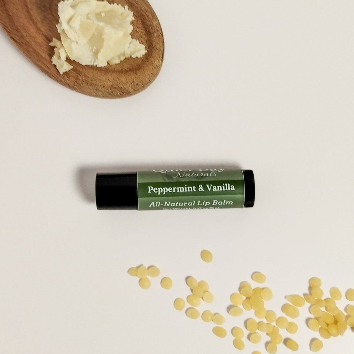 Peppermint and Vanilla lip balm sitting on a white background with shea butter and beeswax around it.