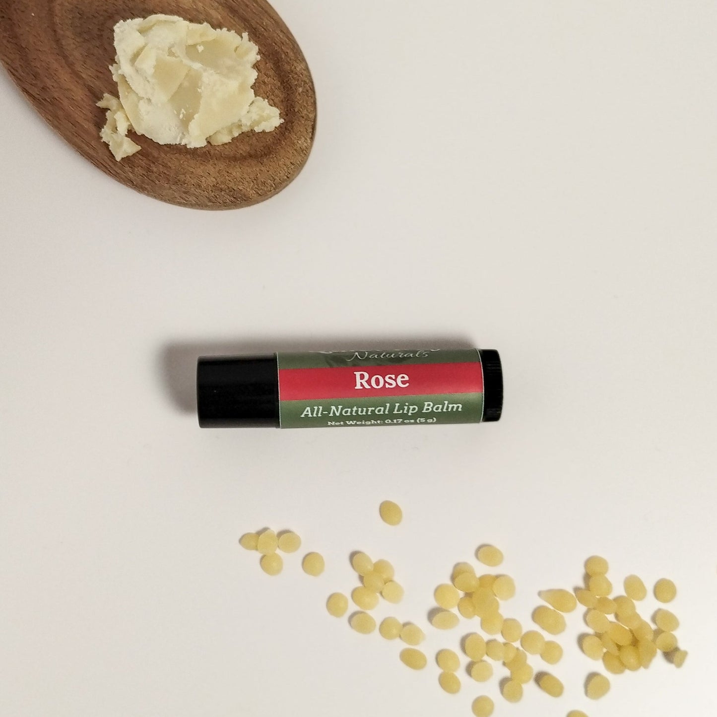 Rose lip balm sitting on a white background with shea butter and beeswax around it.