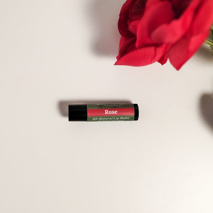 Handmade Natural Lip Balm laying on a white background with a red rose beside it.