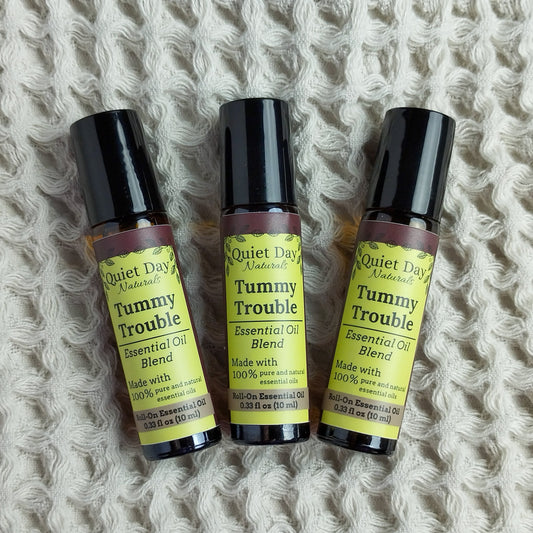 Three Tummy Trouble Essential Oil Rollers against a soft waffle-textured blanket.