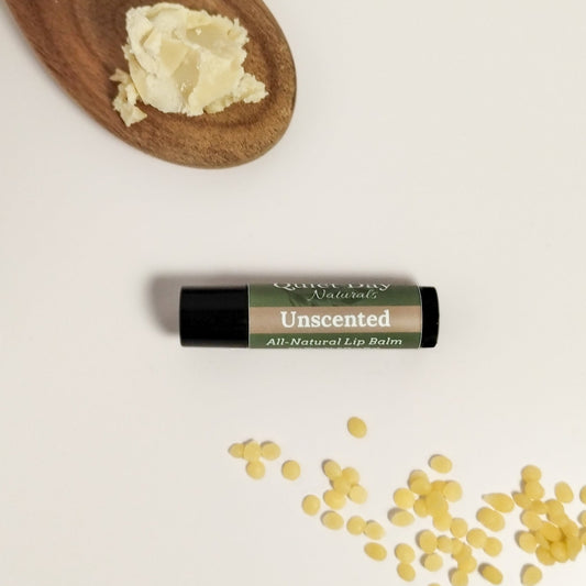 Unscented lip balm sitting on a white background with shea butter and beeswax around it.