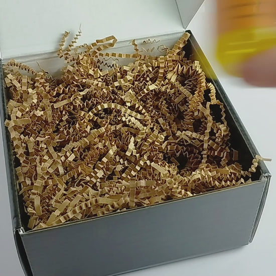 Video showing 3 2oz body oils getting packed into a black box with kraft crinkle paper. Close up showing 3-pack gift set.